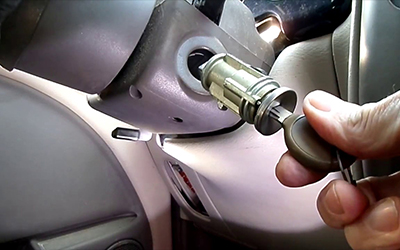 Automotive locksmith repairing damaged car ignition cylinder with specialized tools.